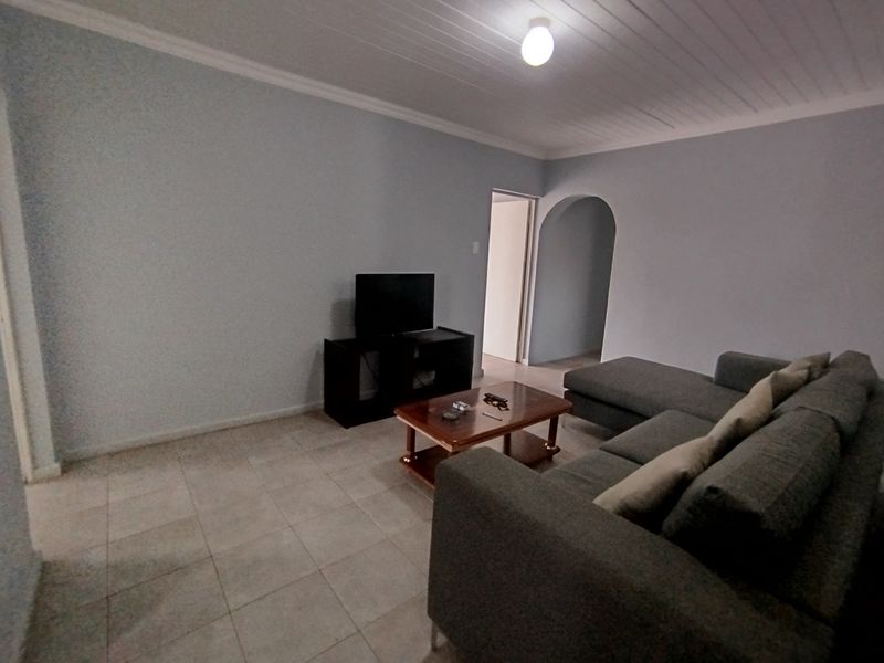 A living room featuring tiled flooring, a tongue and groove ceiling, and an arched doorway leading to an adjacent space.