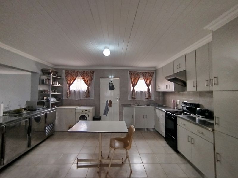 Spacious commercial-style kitchen featuring extensive built-in cabinetry, stainless steel work surfaces, integrated sink, and tiled flooring, suitable for high-volume food preparation.