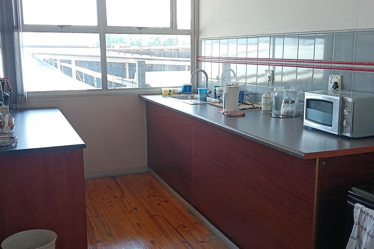 A functional kitchen area featuring dark wood cabinetry, a stainless steel sink, tiled splashbacks, and timber flooring with large windows providing natural light.