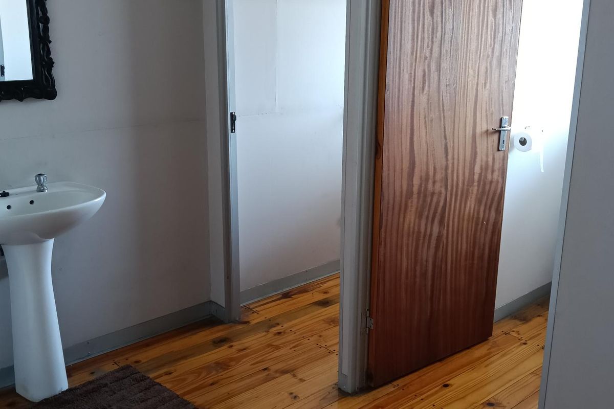 A functional bathroom area featuring a pedestal basin and wooden flooring, with an adjacent doorway leading to a separate toilet compartment.