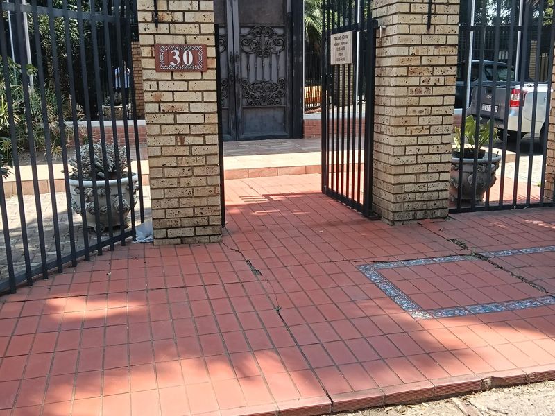 Front entrance of the industrial property featuring a brick pillar gate, metal security fencing, and tiled walkway leading to the main building entrance.