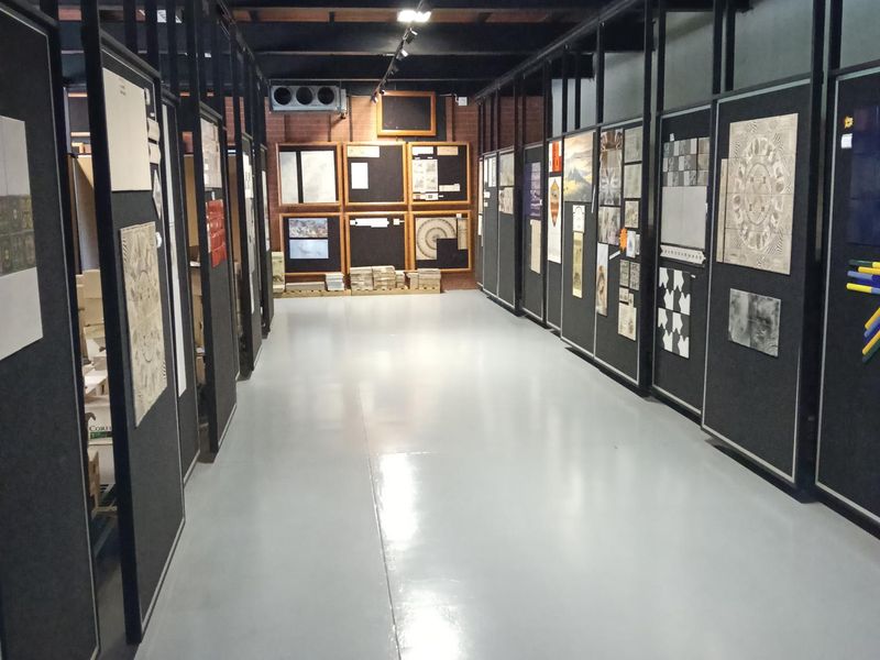 A spacious industrial showroom or utility area featuring high ceilings with exposed beams, polished concrete flooring, and modular display partitions.