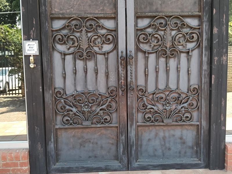 A decorative double wrought iron entrance door featuring intricate scrollwork, set within a dark metal frame and tiled entryway.