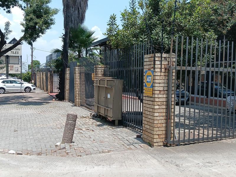 Industrial property exterior featuring a brick perimeter wall, steel security fencing, and gated access with paved driveway area.