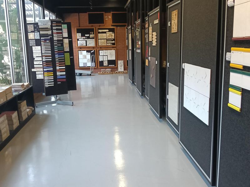 A spacious industrial showroom or utility space featuring polished concrete flooring, exposed timber ceiling beams, and large glass windows along one side.
