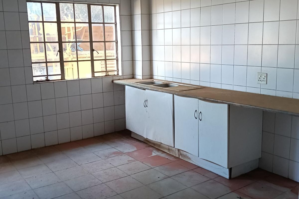 A basic industrial kitchen area featuring tiled walls, a single stainless steel sink, and built-in base cabinetry with a countertop.