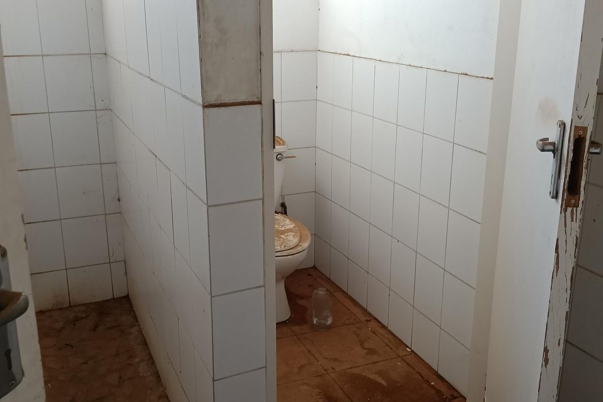A small industrial restroom facility featuring tiled walls and flooring, currently in need of significant maintenance and refurbishment.