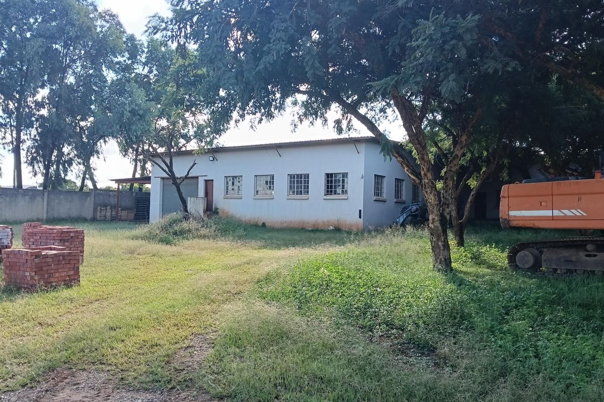 Rear view of an industrial building featuring a roller shutter door, security-barred windows, and a surrounding perimeter wall on a large plot.