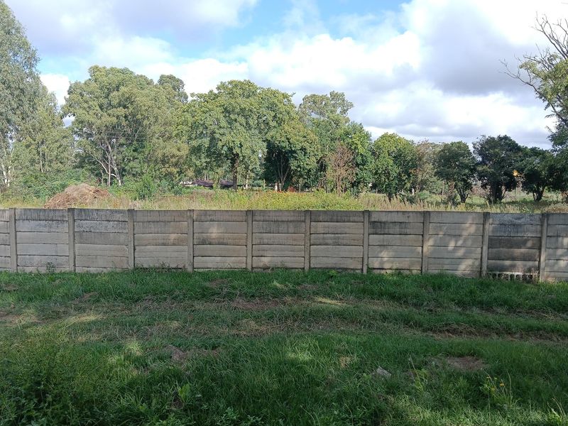 A view of the rear yard featuring a precast concrete boundary wall with mature trees and vegetation in the background.