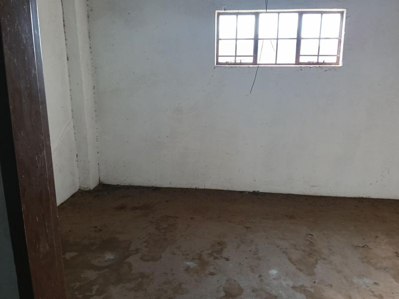 An unfinished industrial utility space featuring bare concrete flooring, plastered walls, and a steel-framed window.