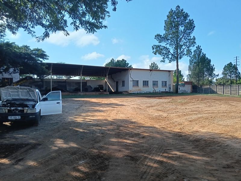 Industrial property featuring a large open-sided shed structure and a spacious unpaved yard, showing signs of significant exterior wear and structural cracking.
