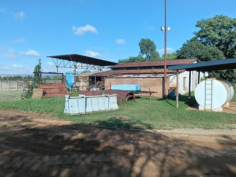 Rear exterior view of an industrial property featuring a metal roof structure, brick building, and outdoor storage tank on a grassed yard.