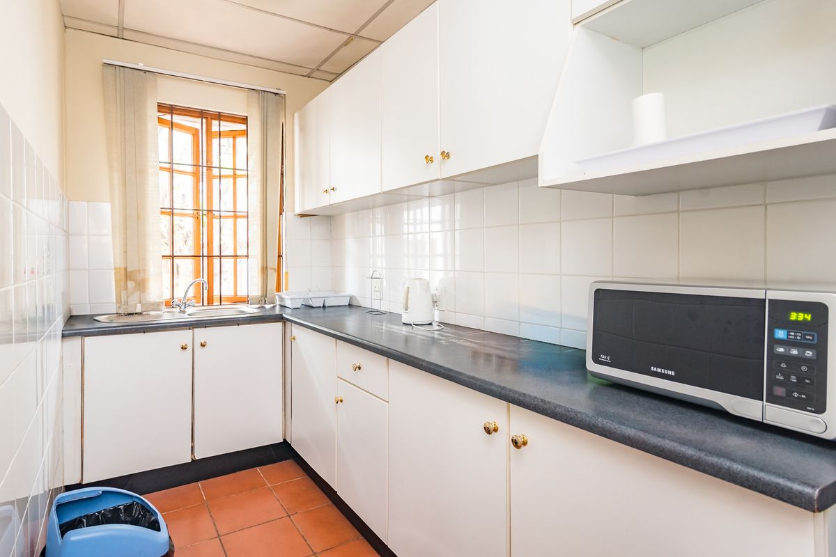 A functional office kitchen featuring white cabinetry, dark laminate countertops, a stainless steel sink, and terracotta floor tiles.