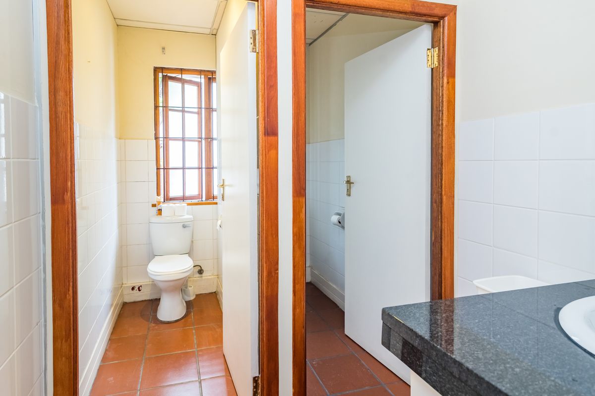 A functional office bathroom featuring tiled flooring, a granite vanity top with basin, and a separate toilet cubicle with security window bars.