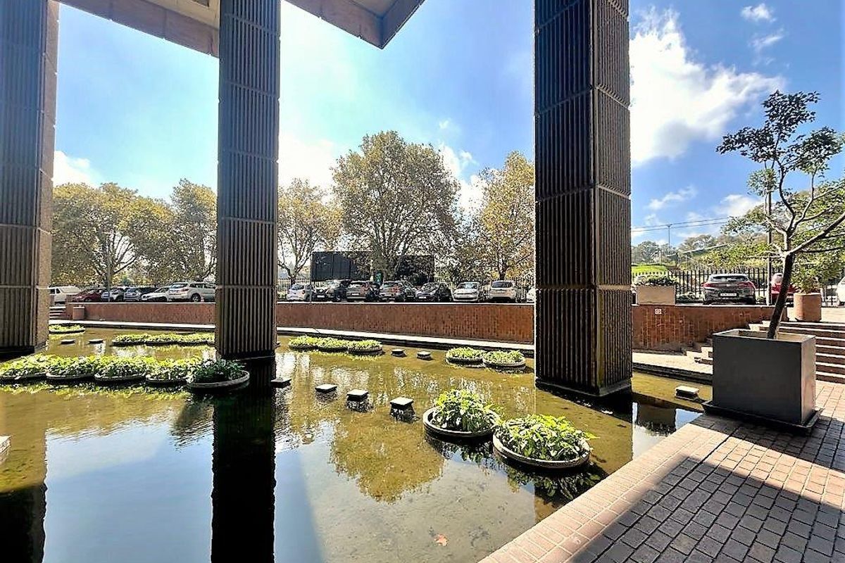 A tranquil outdoor water feature area with architectural concrete pillars, brick paving, and landscaped planters, providing a serene environment for the office complex.