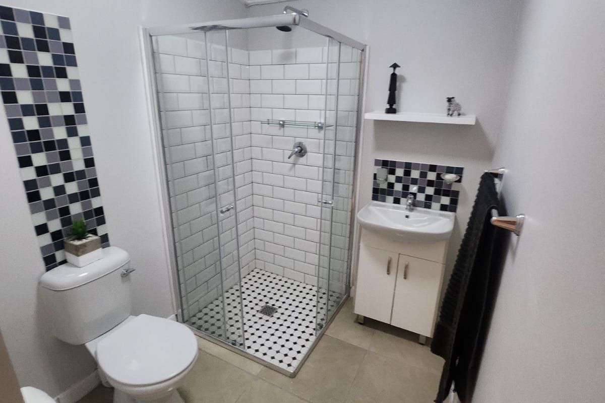 A compact, modern bathroom featuring a glass-enclosed shower, pedestal vanity, and tiled flooring with decorative mosaic accents.