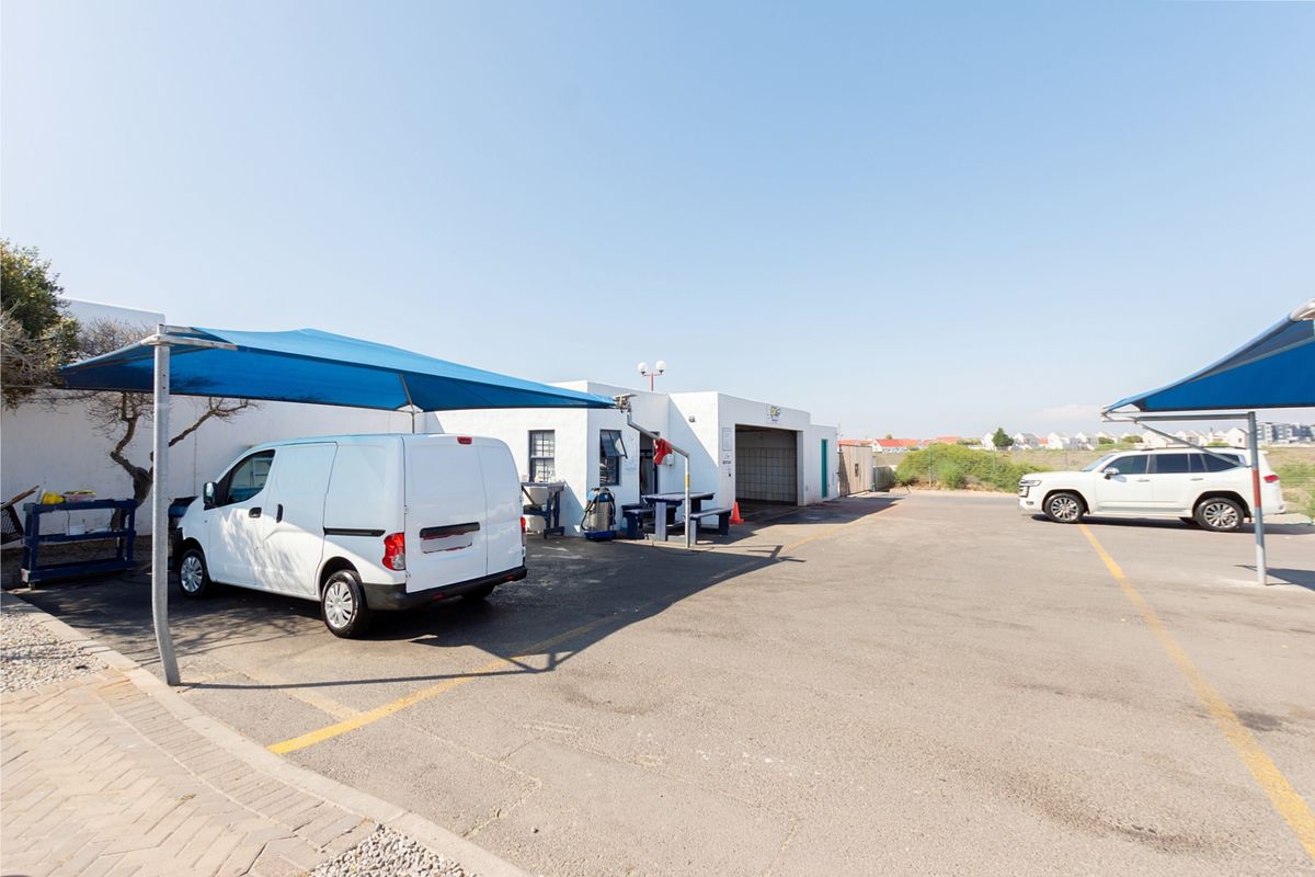 Exterior view of a commercial parking area featuring asphalt surfacing, marked bays, and protective shade sail structures for vehicles.