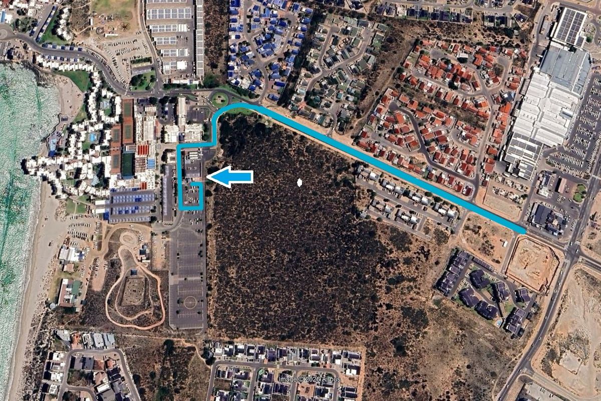 Aerial view showing the property location, surrounding road infrastructure, parking facilities, and proximity to the coastline and residential areas.