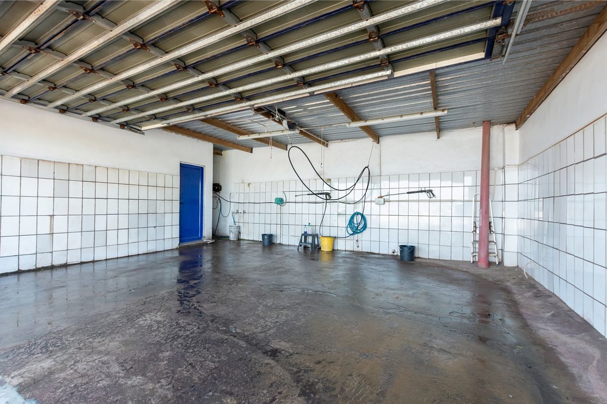 A spacious, functional garage area featuring tiled walls, exposed metal roofing, and durable concrete flooring, suitable for vehicle storage or utility use.
