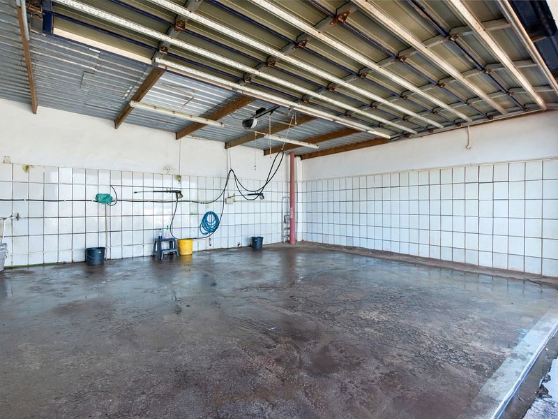 A spacious, utilitarian garage area featuring tiled walls, exposed metal roofing, and a concrete floor, suitable for vehicle storage or workshop use.