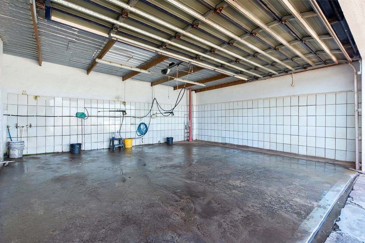 A spacious, utilitarian garage area featuring tiled walls, exposed metal roofing, and a concrete floor, suitable for vehicle storage or workshop use.