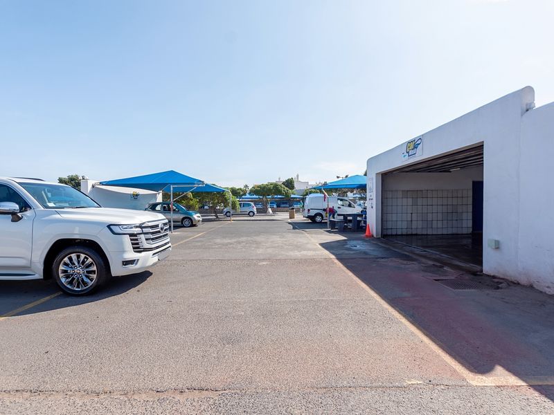Commercial car wash facility featuring an open-air parking area with shade structures and a dedicated tiled wash bay.