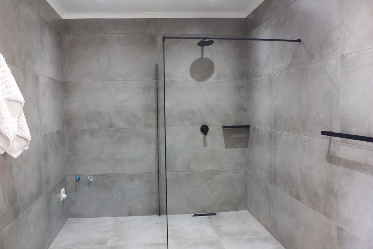 Modern bathroom featuring a walk-in shower with matte black fixtures, large format grey wall tiles, and a glass screen.