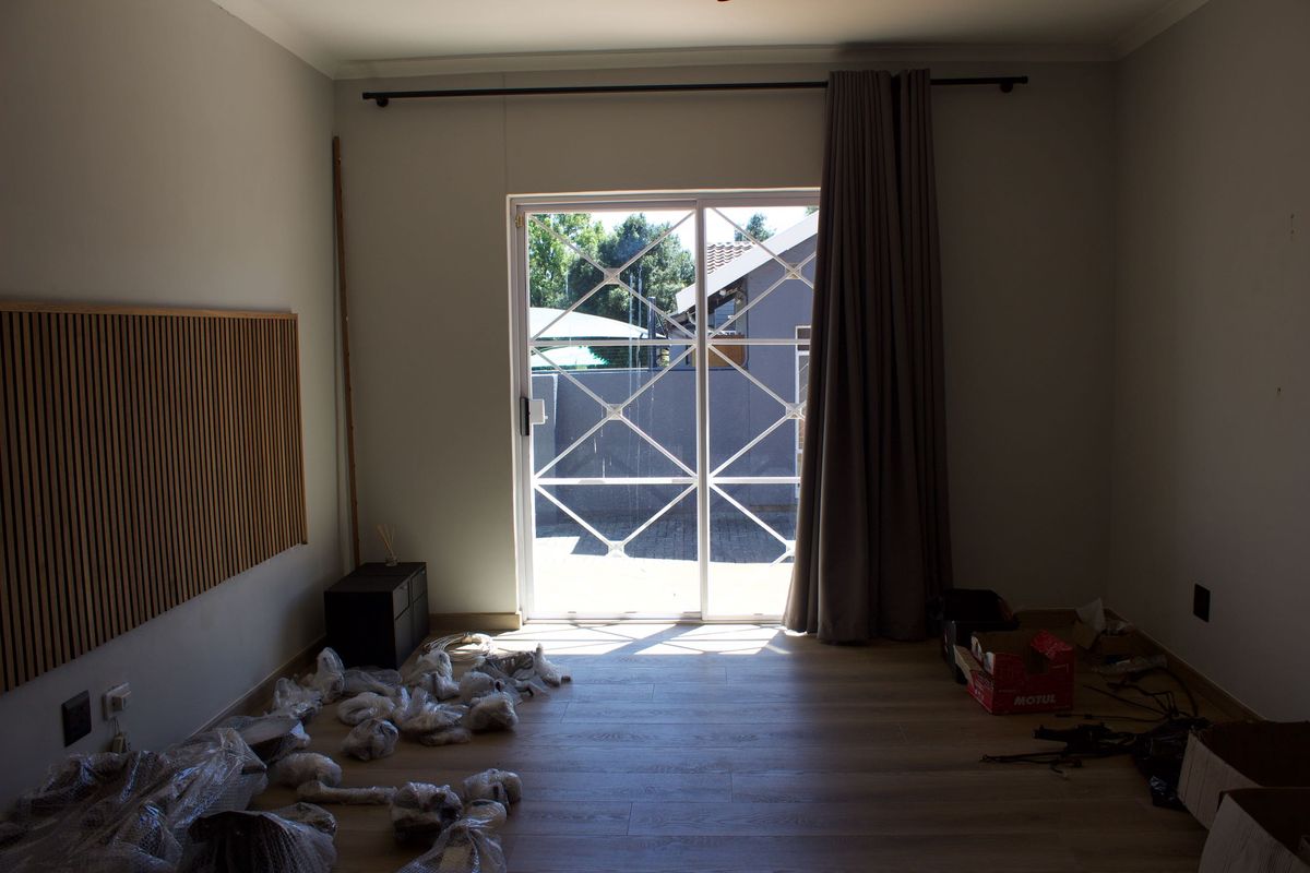 An empty living room featuring light-toned laminate flooring, decorative wall paneling, and a sliding glass door providing access to the exterior.