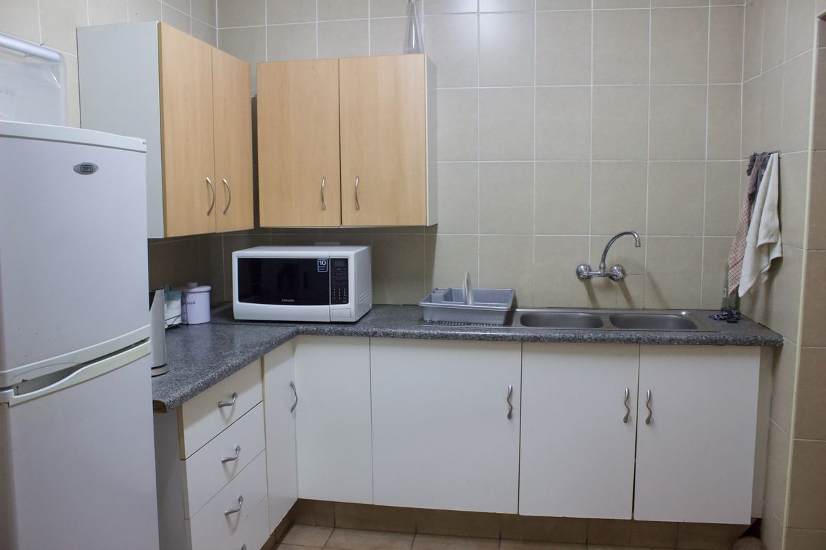 A functional kitchen area featuring laminate cabinetry, granite countertops, a double basin sink, and tiled wall finishes.