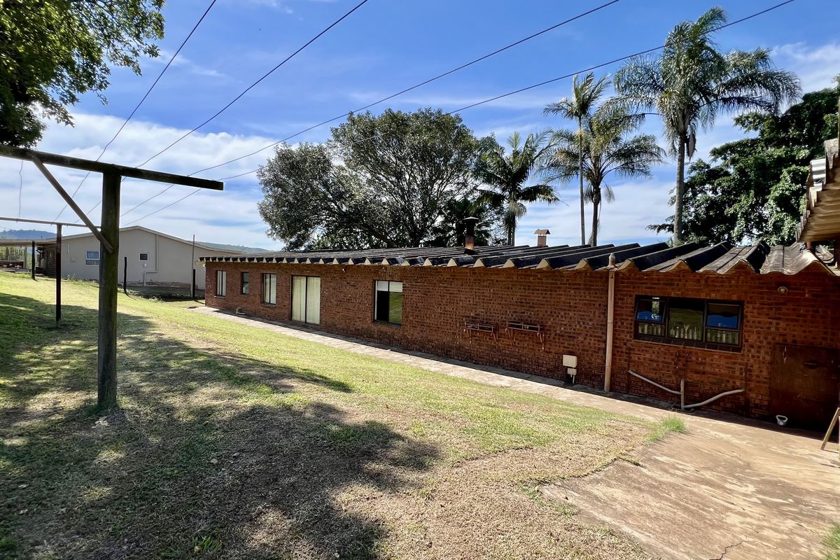 Rear view of a single-story brick farmhouse featuring a corrugated roof, concrete walkway, and surrounding lawn area.