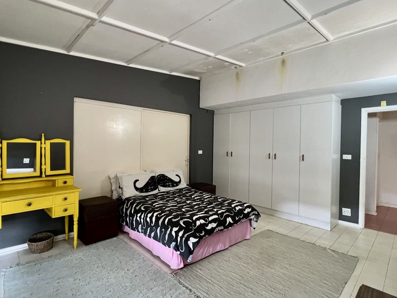 Spacious bedroom featuring built-in cupboards, tiled flooring, and a panelled ceiling, requiring some maintenance to address visible ceiling water staining.