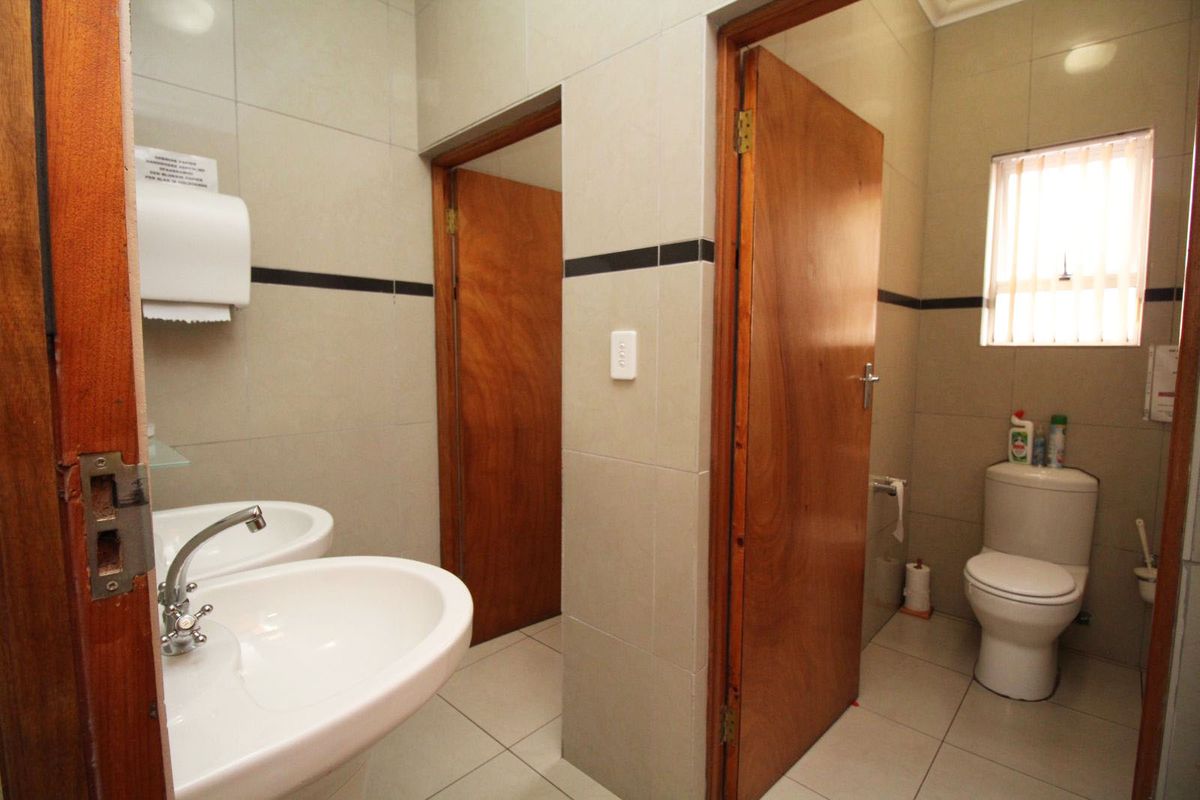 A functional office bathroom featuring dual pedestal wash basins, ceramic tiling throughout, and a separate toilet cubicle with wooden doors.