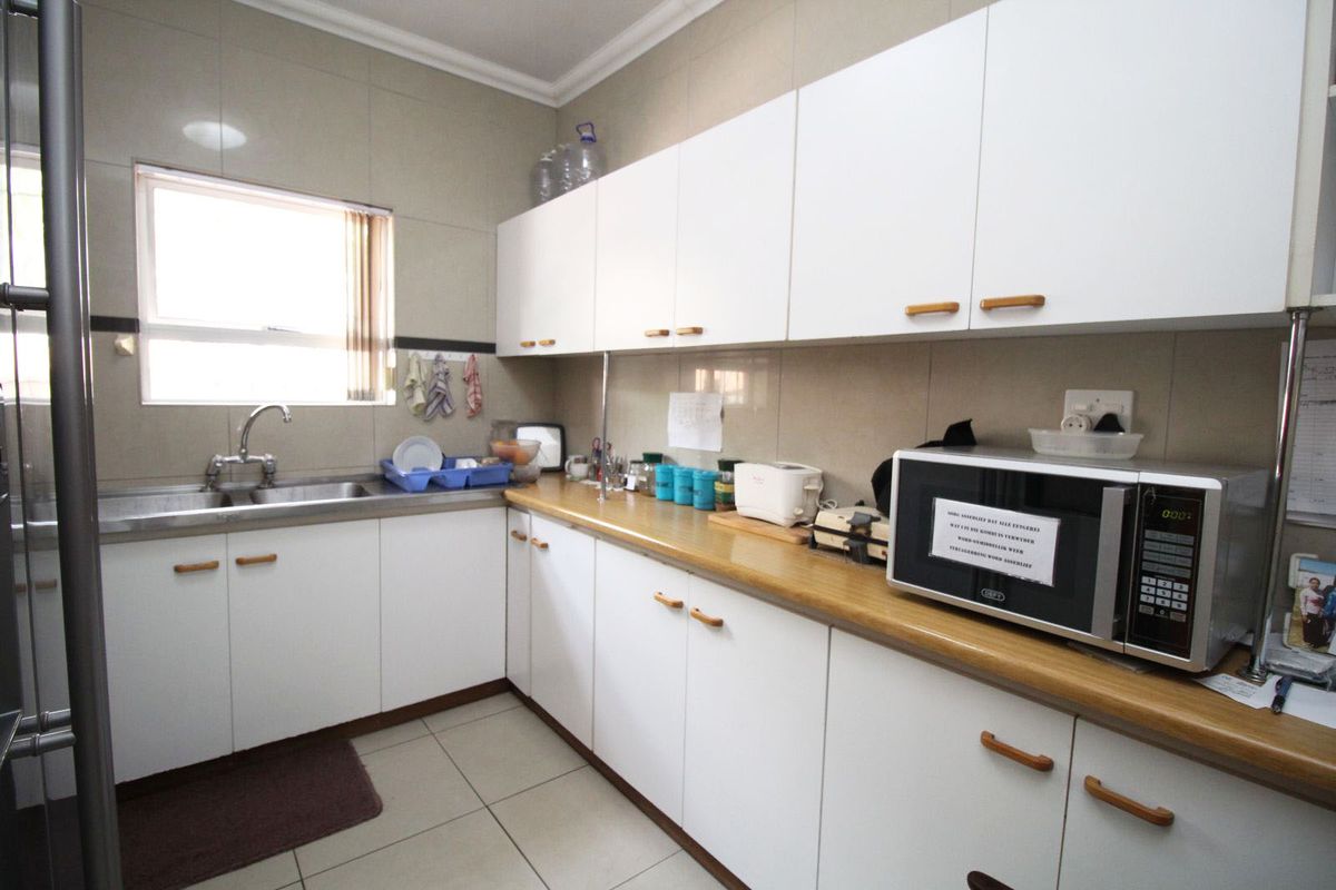 A functional kitchen area featuring white built-in cabinetry, laminate countertops, a stainless steel double sink, and neutral tiled finishes.