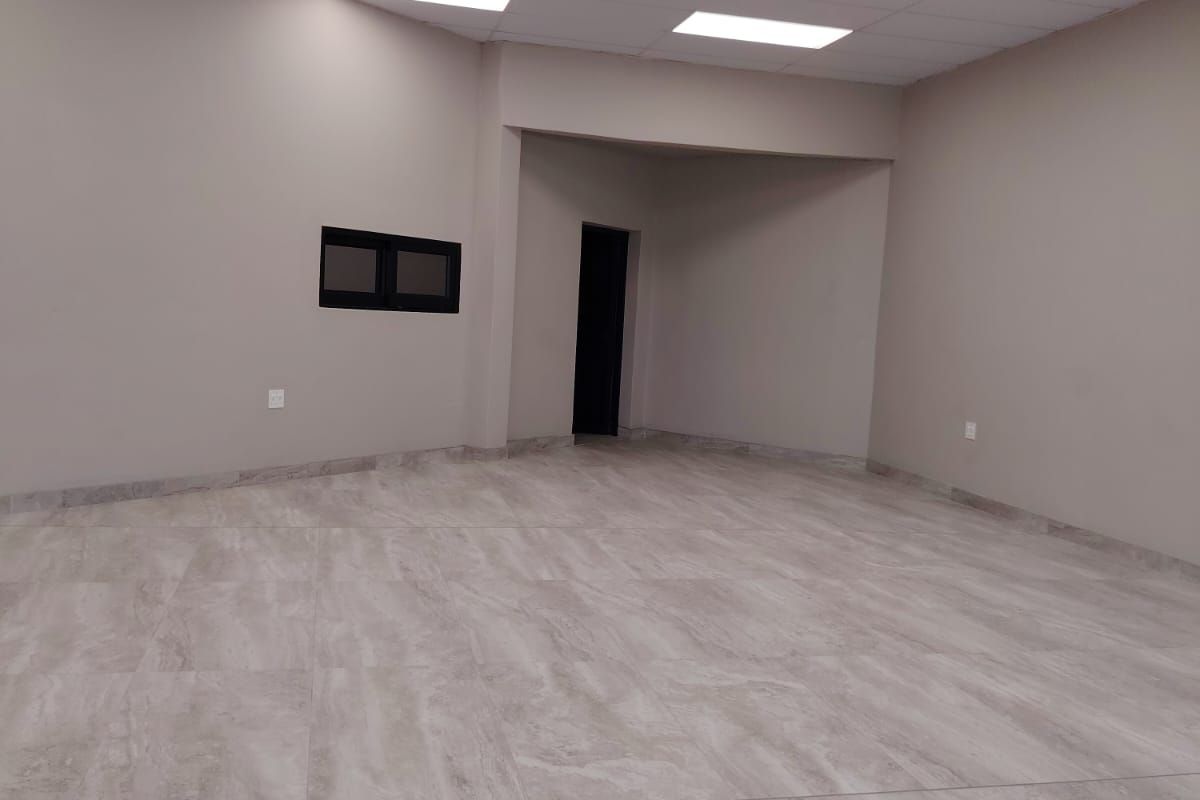 A spacious, empty office area featuring modern tiled flooring, a clean drop ceiling with recessed lighting, and neutral wall finishes.