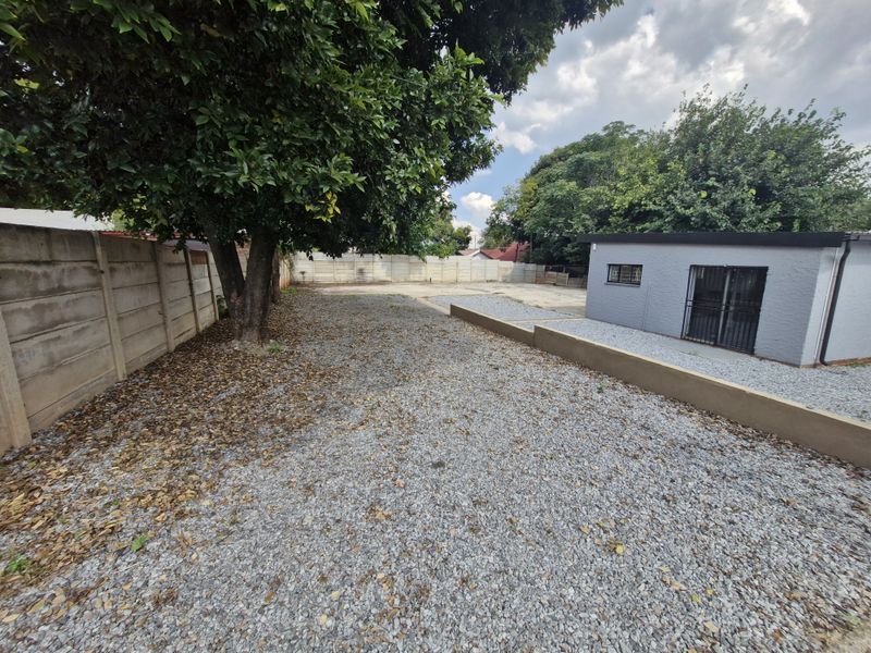 A rear exterior area featuring a gravel surface, precast concrete boundary walls, and a small outbuilding with security features.
