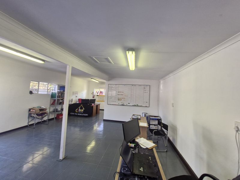 A functional commercial office space featuring tiled flooring, fluorescent lighting, and a wall-mounted whiteboard, suitable for administrative or business operations.
