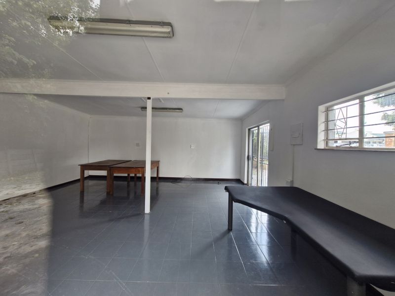 An open-plan commercial office space featuring tiled flooring, fluorescent lighting, and a security-barred window, providing a functional and versatile workspace.