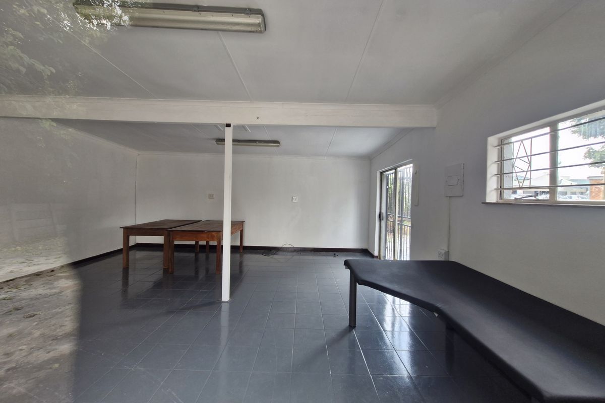 An open-plan commercial office space featuring tiled flooring, fluorescent lighting, and a security-barred window, providing a functional and versatile workspace.