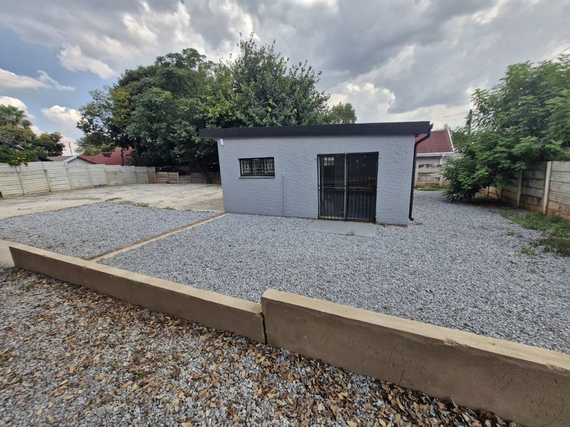 Rear view of a detached commercial outbuilding featuring a grey textured facade, security gate, and gravel-landscaped yard with a concrete retaining wall.