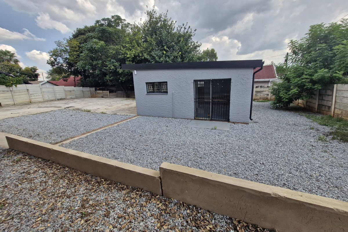 Rear view of a detached commercial outbuilding featuring a grey textured facade, security gate, and gravel-landscaped yard with a concrete retaining wall.