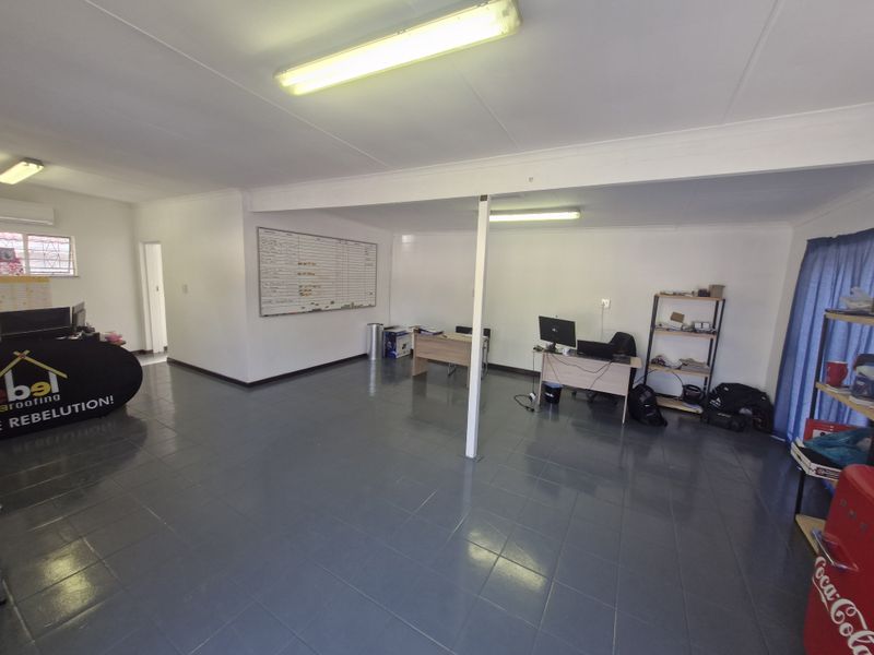 Open-plan commercial office space featuring tiled flooring, functional fluorescent lighting, and a central support column, suitable for a professional work environment.