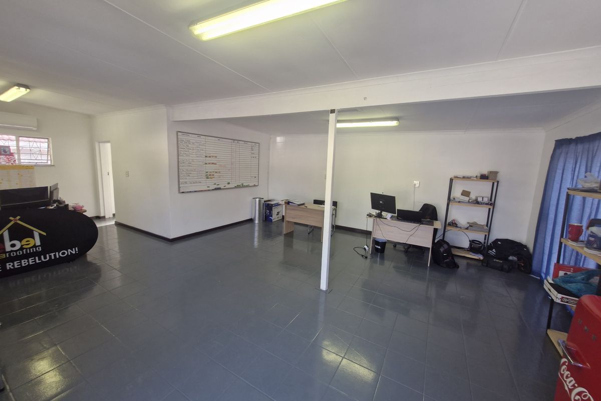 Open-plan commercial office space featuring tiled flooring, functional fluorescent lighting, and a central support column, suitable for a professional work environment.