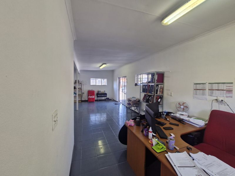 A functional commercial office space featuring tiled flooring, fluorescent lighting, and a sliding glass door providing natural light and access.