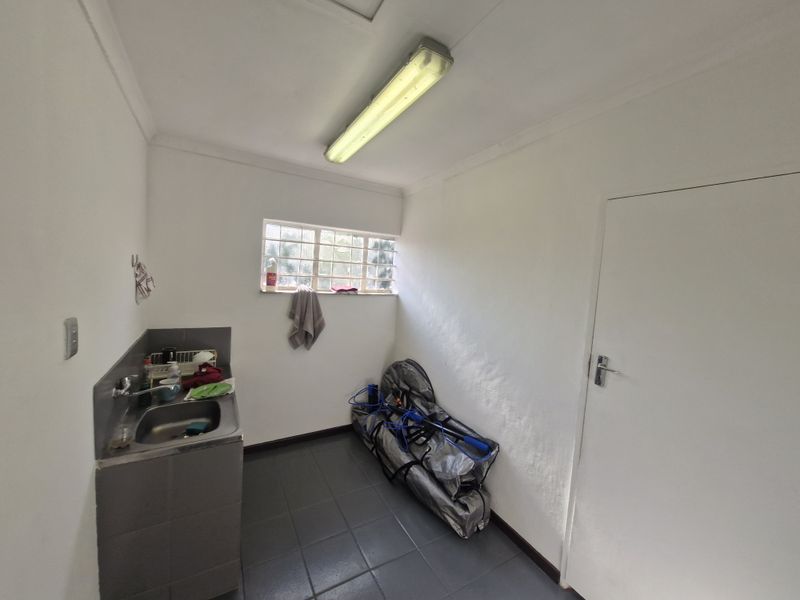 A functional laundry room featuring a stainless steel sink, tiled splashback, and tiled flooring, providing a practical utility space for the property.
