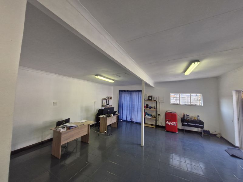 Open-plan commercial office space featuring tiled flooring, fluorescent lighting, and security bars on the window.