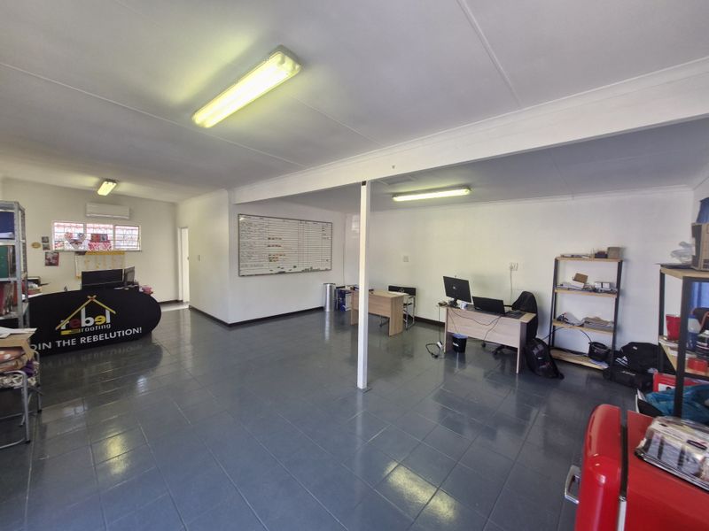 Open-plan commercial office space featuring tiled flooring, fluorescent lighting, and a central support column, suitable for a professional work environment.