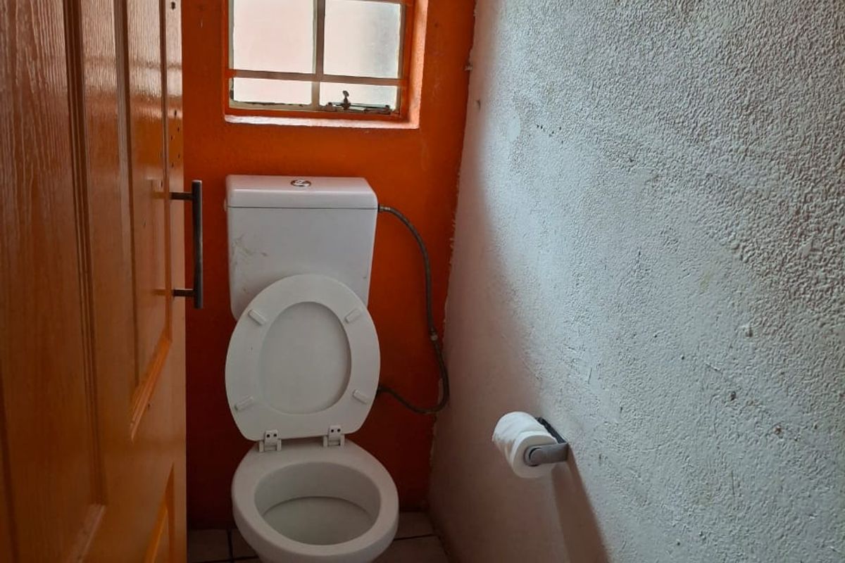 A compact bathroom featuring a standard toilet, tiled flooring, and a small window, requiring cosmetic updates to improve the overall aesthetic.