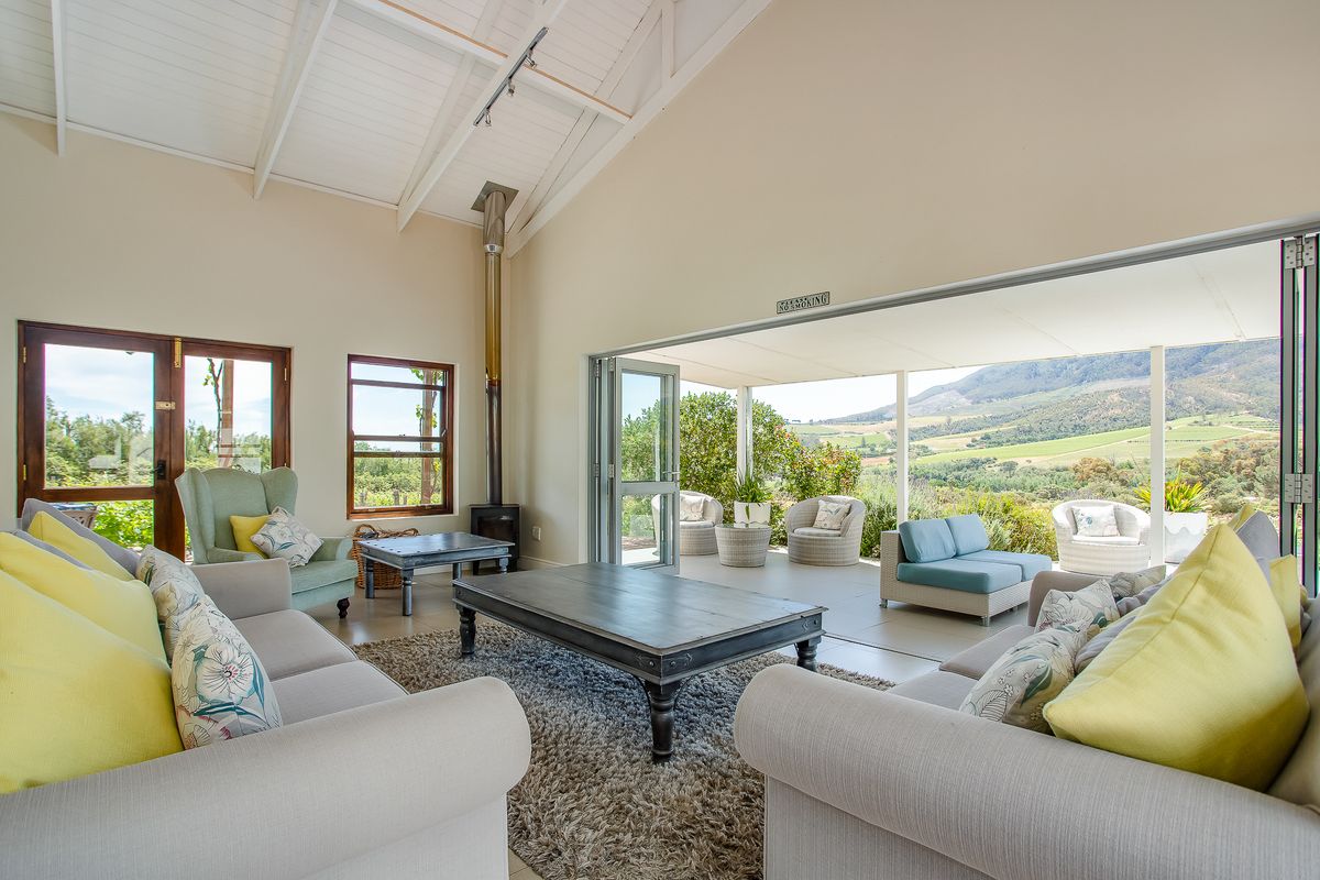 Spacious living room featuring a vaulted ceiling with exposed rafters, a wood-burning stove, and large stacking doors opening to a scenic patio.