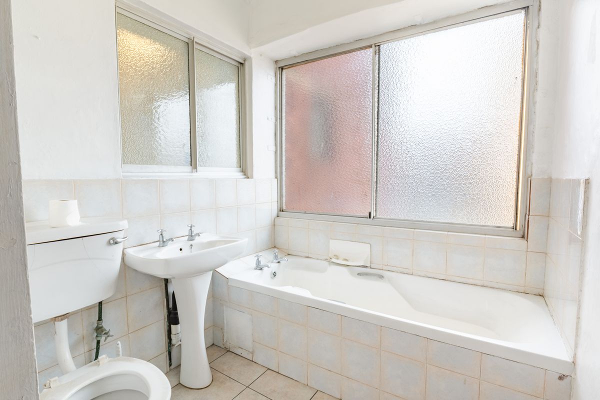 A dated bathroom featuring a pedestal basin, built-in bathtub, and ceramic tiling throughout, requiring modernization to improve its overall condition and appeal.