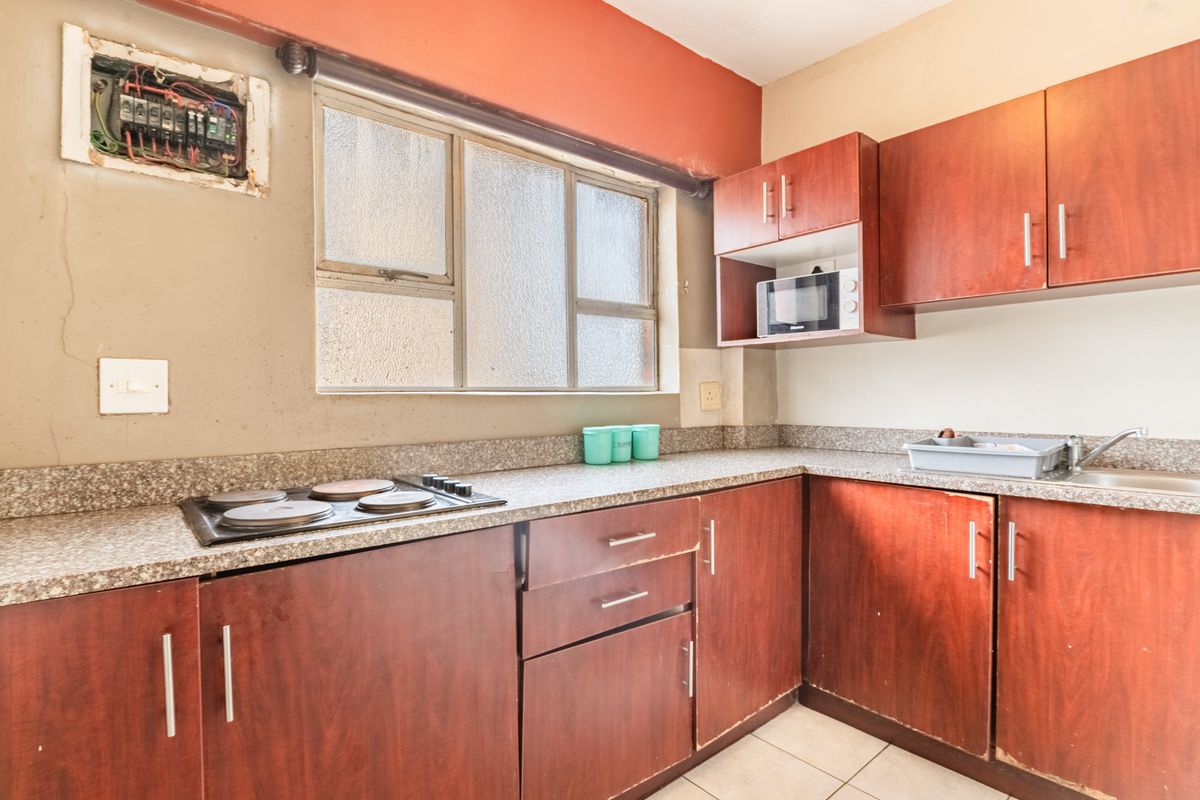 A compact kitchen featuring laminate cabinetry, an electric hob, and a stainless steel sink, requiring cosmetic updates and electrical board cover installation.